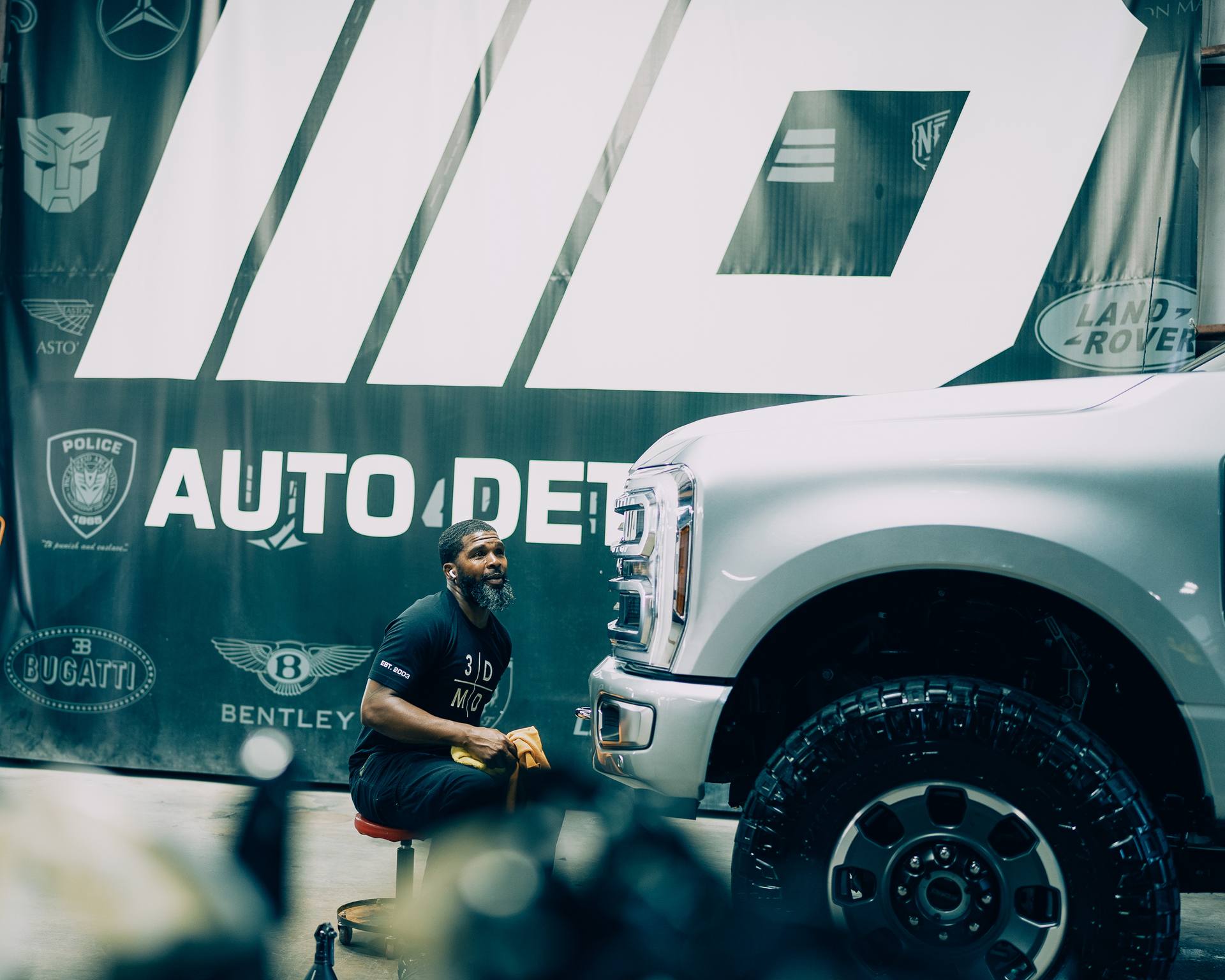 David of 3D Auto Detailing working in front of the IIID shop banner